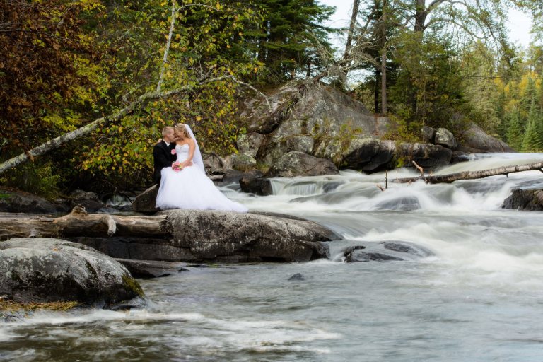 Wedding couple sitting on the stone beside a rushing river